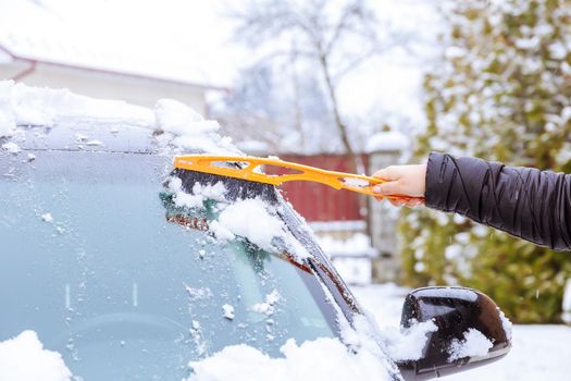 A car covered with snow. A man with his hand cleans the windshield of the car from the snow with special brushes. Frosty weather.