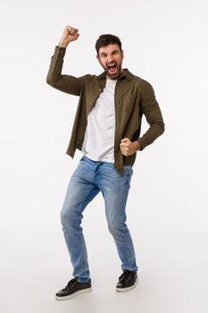 Achievement, success and prize concept. Vertical full-length studio shot pleased and rejoicing male with beard in casual outfit, celebrating good news, fist pump and dancing, smiling upbeat.