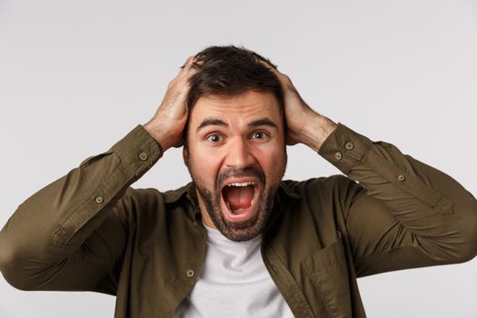 Man in panic and fear losing mind, feeling upset and alarmed. Troubled puzzled and depressed handsome bearded man grab head and shouting, cant deal with problems, standing white background.