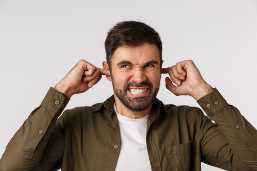 Cant stand this annoying stupid neigbours with theis sound system. Angry and irritated, annoyed bearded guy cursing and grimacing annoyed, closed ears with fingers stare up, disturbed loud music.