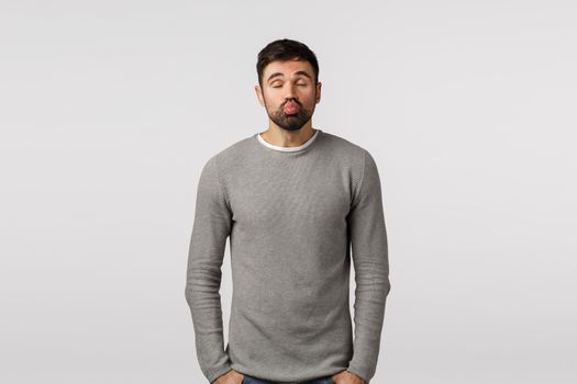 Funny bearded boyfriend asking for kiss with hilarious expression, pouting lips and move forward with closed eyes as want make-out, standing white background in grey sweater. Valentines day concept