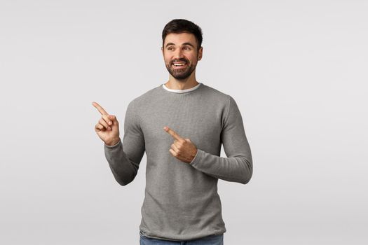 Pleased charming lucky young handsome male, adult in grey sweater, pointing looking left, observe cute scene, picked variant, see nice choice, happy and charmed, smiling satisfied.
