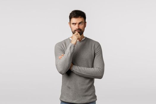 Hmm touch decision. Thoughtful and serious pensive adult caucasian boyfriend with beard, grey sweater, trying think up ideas for valentines gift, touch chin, look upper left corner pondering.
