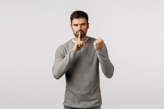 Shut up or else. Threatening angry and serious scary bearded man demand keep silent, dont tell anyone, threaten victim with shaking fist, press index finger to lips, untell, hushing, white background.