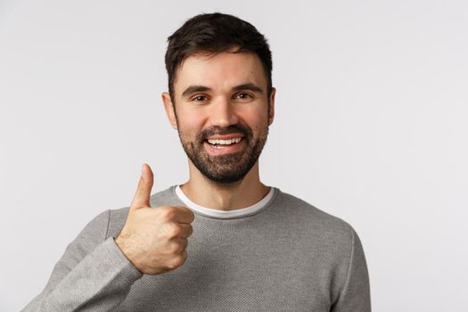 Close-up shot reliable and pleased smiling, happy man with beard in grey sweater, show thumb-up give approval, like or recommend company service, think everything excellent, leace positive feedback.