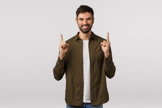 Time to make choice, here what you looking for. Attractive pleasant bearded smiling guy in coat, pointing fingers up, give advice, talking about product, corporate promo, recommend shopping site.