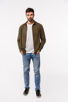 Vertical full-length shot sassy and confident modern man in coat, jeans streetstyle outfit, holding hands in pockets, looking assertive, smiling, getting ready business appointment, white background.