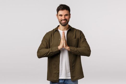 Cheerful, relaxed and friendly smiling caucasian man press palms together in pray, grinning, meditating or finish yoga practice, bowing to express gratitude sensei, standing white background.