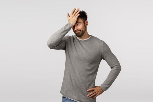 So dumb. Forgetful and displeased, tired bearded man in grey sweater, facepalm, punch forehead as forgot important task, hear lame stupid idea, smirk annoyed, standing embarrassed white background.