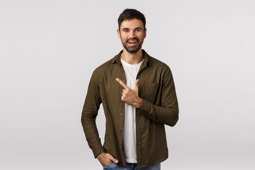 Cheerful, friendly handsome bearded guy in modern outfit, pointing left, introduce person to friends or recommend place shop, picking product, smiling gladly, making reservation, white background.