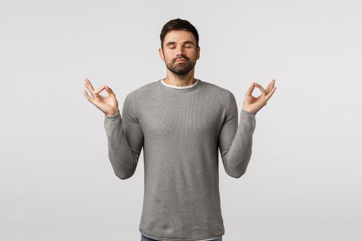 Patience, relaxation and meditation concept. Peaceful young handsome bearded guy broaden mind and body, feeling zen, raise hands mudra gesture, practice breathing yoga with closed eyes.