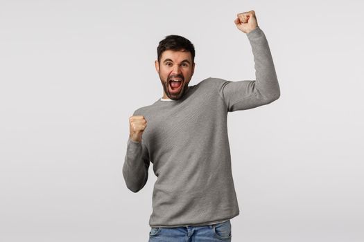 Hooray. Excited and happy man cheerfully lift one hand, fist pump like champion, celebrate win of team scored goal, achieve prize, win huge bid in sport lotto, standing white background triumphing.