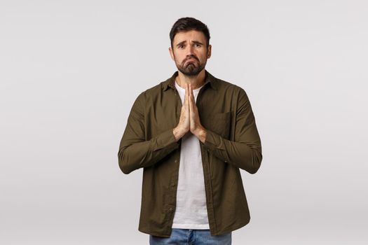 Sad, gloomy and miserable, depressed young man need help, begging for forgiveness, apologizing, press palms together in pray, supplicationg, frowning and pulling grimace, white background.