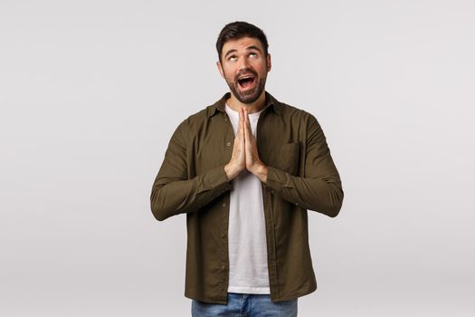 Dreamy, hopeful cute caucasian bearded man believe god, want dream come true, press palms together over chest, hope wish fulfill, looking up happy and optimistic, anticipate relish good deal.