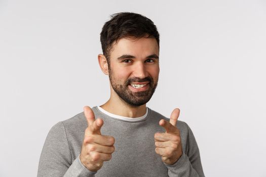Gotcha. Cheeky, enthusiastic, handsome bearded caucasian male in grey sweater, pointing camera finger pistols and smiling joyfully, congratulate friend, praise achievement, standing white background.