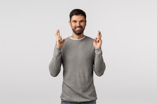 Anticipation, hope and emotions concept. Cheerful faithful good-looking bearded guy feeling lucky, cross fingers good fortune and smiling, expect good news, ancitipate win, standing white background.