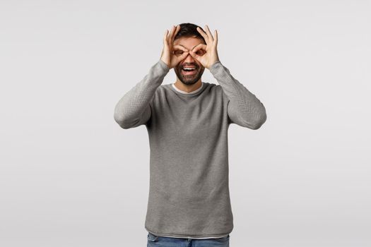 Funny, playful and amused cute bearded father fool around, making glasses or binocular gesture with fingers over eyes, smiling joyfully, standing goofy and optimistic, feeling happy having fun.