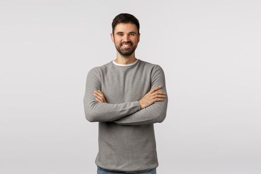 Hire, employement and company concept. Cheerful good-looking caucasian bearded man in grey sweater, cross arms chest, smiling pleased and self-assured, hr interviewing employee, white background.