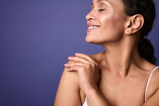 Close-up beauty portrait of self-confident middle aged African woman with perfect clean shiny healthy skin, hugging herself, isolated over violet background with copy space. Skin and body care concept