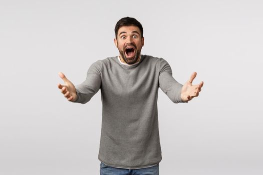 Guy rushing forward to catch vase from falling and breaking. Worried and panicking young bearded man in grey sweater run raise hands to support, hold something, open mouth scream shocked.
