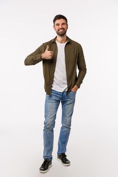 Approval, acceptance and advice concept. Vertical shot full-length attractive modern masculine bearded man in jeans, light coat, show thumb-up in like gesture, recommend product, love idea.