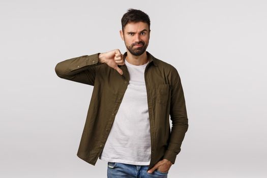 Man express disagreement and disappointment. Upset and displeased serious skeptical male friend show thumb down in dislike, disapproval, grimacing unsatisfied, stand white background.