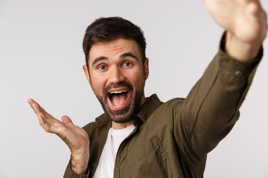 Happy and cheerful, glad young man introduce something as talking on online record video and describe product, hold smartphone extended arm, taking selfie, pointing left, white background.