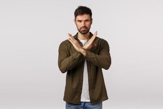 Stop right now. Angry and annoyed serious bearded man demand quit, forbid action, make cross gesture across body and frowning with strict expression, prohibit action, white background.