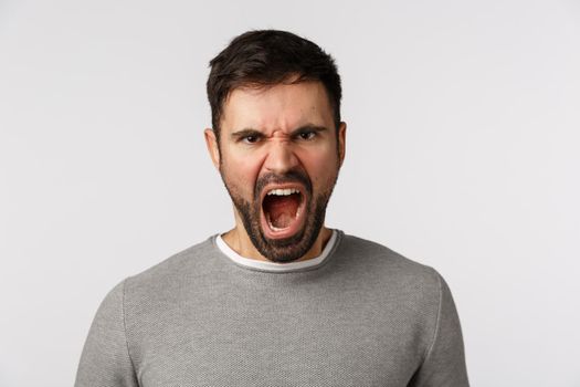 Hateful and pissed angry shouting bearded man with scary grimace, frowning express scorn and disdain, complain showing anger, furiously scream, standing white background outraged. Copy space