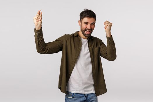 Celebration, triumph and joy concept. Happy cheerful caucasian male with beard, raising hands and dancing happily, achieve goal, got appoval or hired awesome job, become champion, winning.