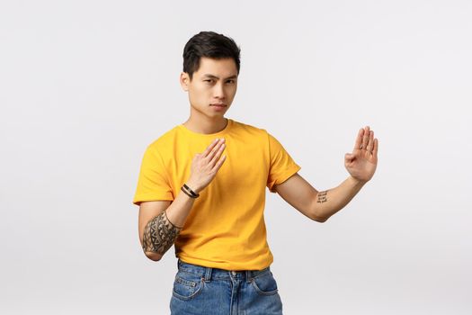 Sensei will teach you some moves. Daring and confident good-looking asian tattooed hipster guy in yellow t-shirt, standing in martial arts, judo pose as if practicing fighting skills, look camera.