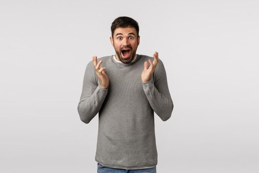 Impressed and excited man receive great news. Speechless ecstatic good-looking bearded guy in grey sweater realise he won, clasping hands cant believe own luck, feeling happy and surprised.