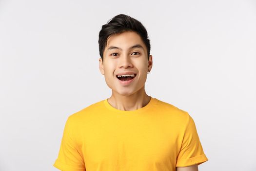 Close-up studio shot, amused cute asian guy smiling as seeing something wonderful, look enthusiastic and impressed, attend beautiful interesting performance, standing entertained white background.