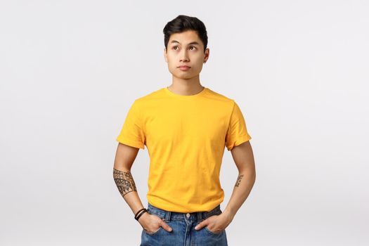 Annoyed asian handsome guy losing his temper, looking away with angry irritated expression, hold hands in pockets, want leave place, standing bothered and thoughtful white background.