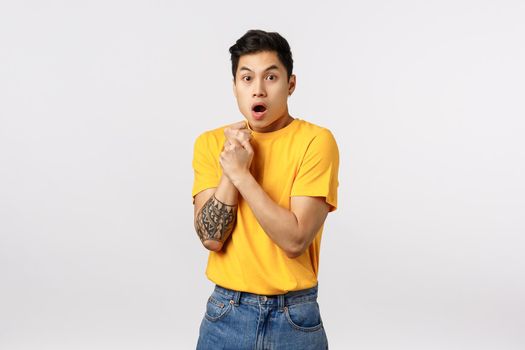 Sensetive and shocked, scared young asian guy with tattoos, pull hand back, press arm to chest insecure and afraid, gasping open mouth, look like victim at someone abuse him, stand white background.