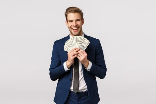 Guy bragging with money. Attractive blond bearded businessman in classic suit, holding lots cash, showing dollars and smiling satisfied, won lottery, sport bet, standing white background pleased.