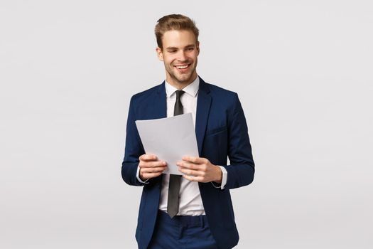 Business, elegance and success concept. Handsome stylish modern businessman in classic suit, tie, holding documents, paper and laughing, smiling look away, express confidence, white background.