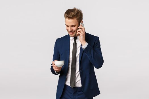 Office, corporate and business concept. Confident, good-looking elegant male entrepreneur starting own business deal with partners over phone, holding smartphone, calling friend, drink coffee.