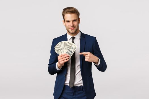 Check this out, how success looks like. Handsome businessman with cash in hands, pointing money and smiling confident, bragging, discuss how manage business, starting own company. Copy space