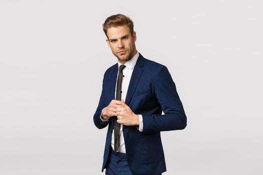 Determined, confident businessman in suit, fixing jacket, looking sassy and pleased camera, signed good deal, feeling lucky and self-assured, manage business, standing white background. Copy space