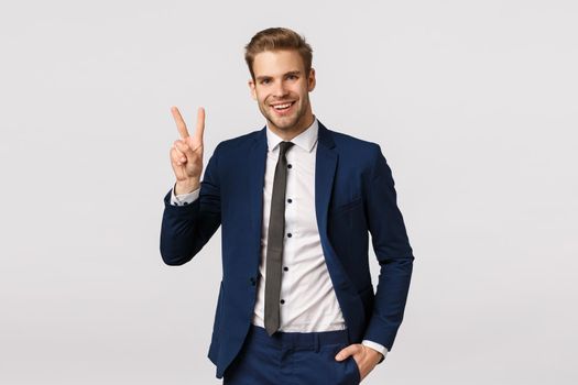 Charming, wealthy good-looking blond bearded guy in classic suit, showing peace sign, smiling joyfully, telling team they made deal, businessman pleased how good offer went, white background.
