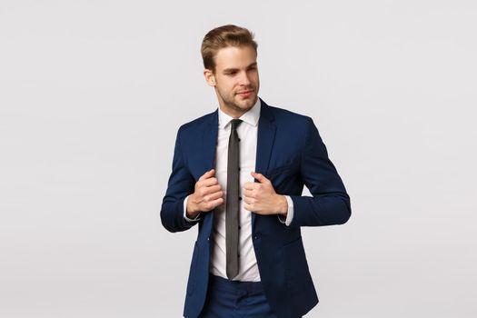 Success, confident and business concept. Attractive, handsome bearded blond guy in classic suit, adjusting jacket, looking at himself mirror, try new outfit for office meeting, white background.