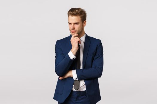 Thoughtful smart and focused young blond bearded man in formal classic suit, having deep thought, touching chin look away, thinking about solution, make plan, brainstorm during meeting.