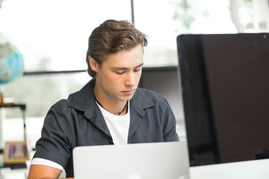 Young man in casual sitting at desk and working on computer