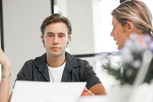 Young colleagues sitting at desk and having discussion in bright office