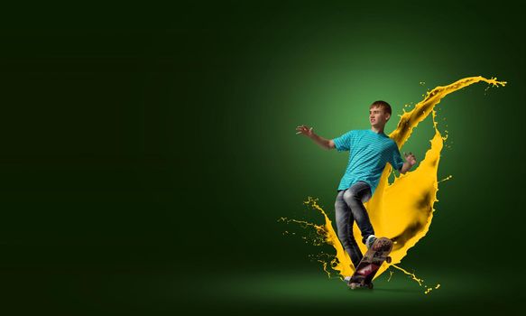 Young guy riding skateboard and paint splashes from under wheels