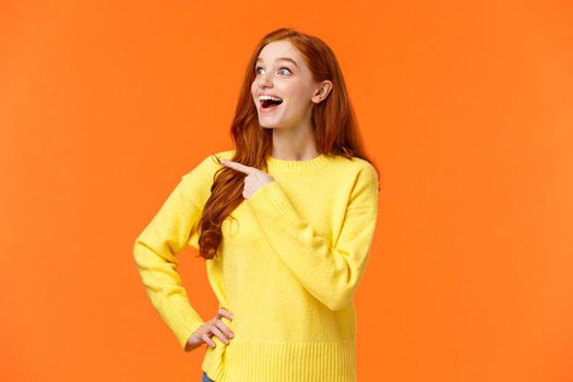 Look at that, wow. Impressed and fascinated, astonished cute redhead woman stare and pointing left with excited, happy smile, shoppaholic adore winter holiday sales, express interest and admiration.