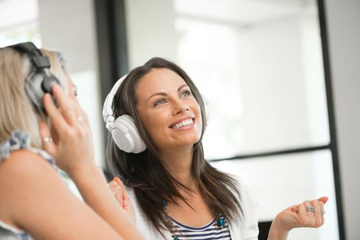 Two pretty women in headphones sitting at desk in office