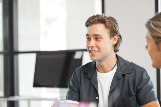 Young colleagues sitting at desk and having discussion in bright office