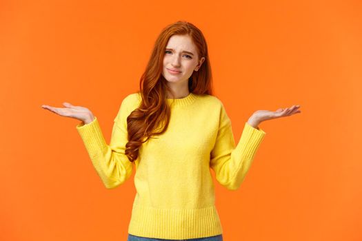 Girl hearing ridiculous stupid question. Careless and unbothered cute redhead woman in yellow sweater, shrugging with hands raised sideways, frowning grimacing indecisive, feeling confused.